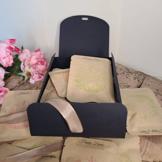 Set of 'Happy Hours' bags with a black holder on a textured surface with pink flowers in the background.